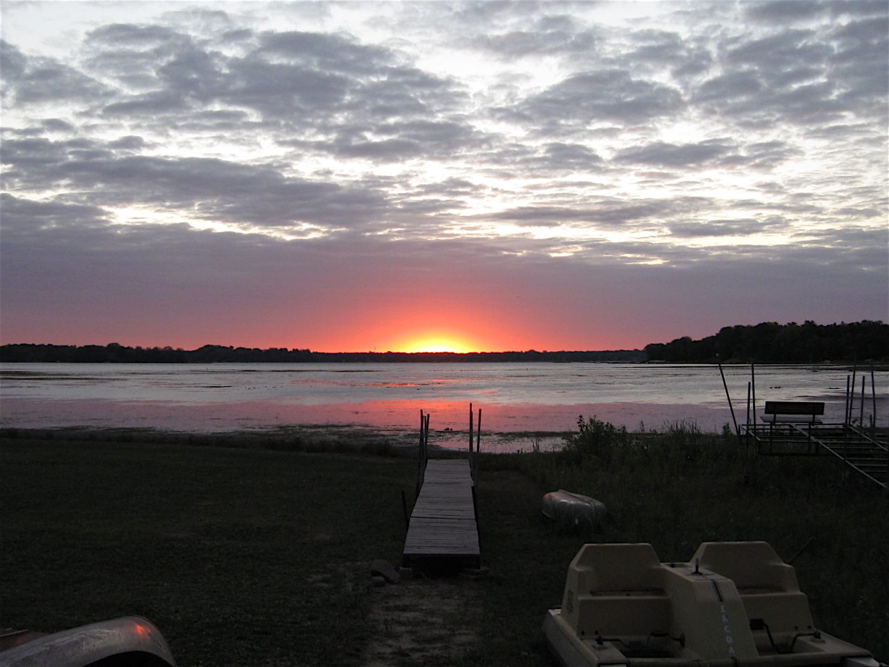 Sunset over lake with cloudy sky.