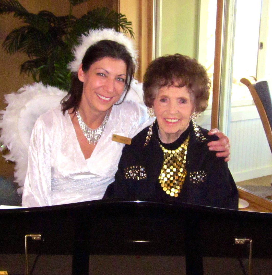 Two women smiling by a piano.