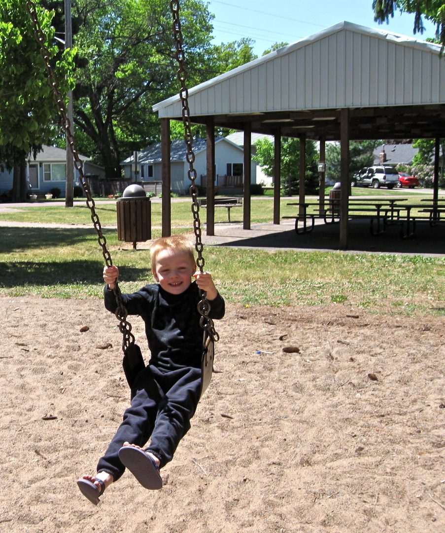 Child swinging at playground, sunny day.
