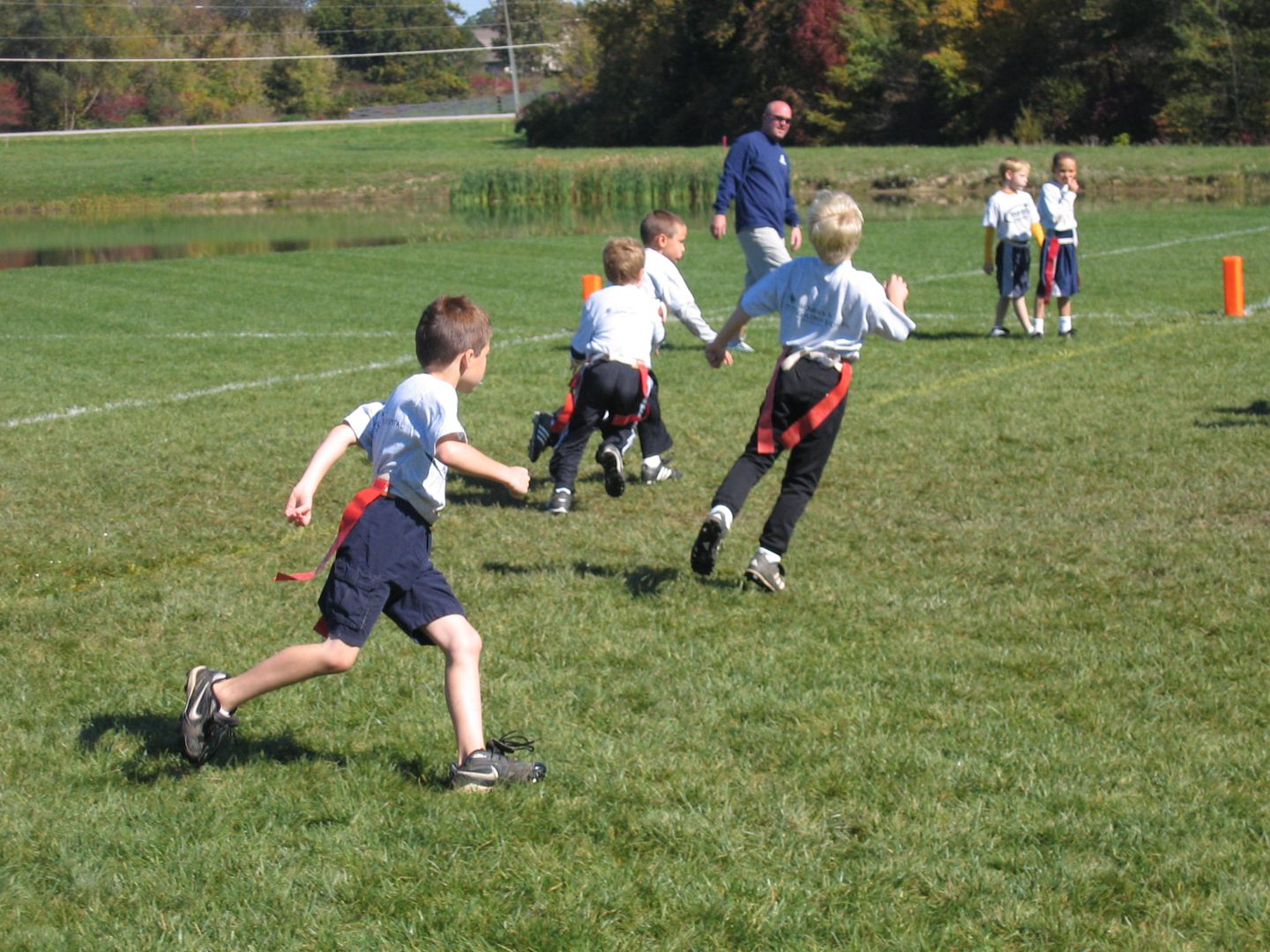 Children playing flag football on grass field.